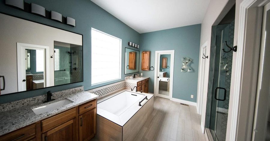 Blue-walled bathroom with double vanity, marble counters, and large mirror